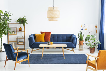 Retro armchairs with wooden frame and colorful pillows on a navy blue sofa in a vibrant living room...