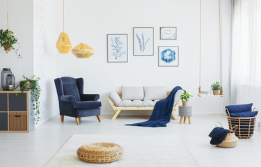 Real photo of a living room interior with blue accents, wicker pouf on the floor and poster collection