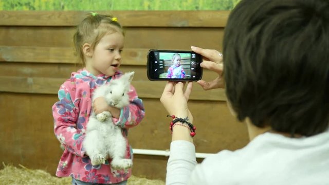 Mom take photo picture via smart phone of little daughter child with rabbit