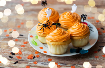 food, baking and holidays concept - cupcakes or muffins with halloween party decorations and candies on plate