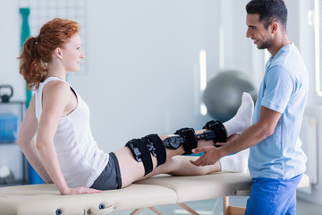 Smiling doctor and woman with leg injury during treatment in the hospital