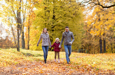 family, season and people concept - happy mother, father and little daughter walking at autumn park