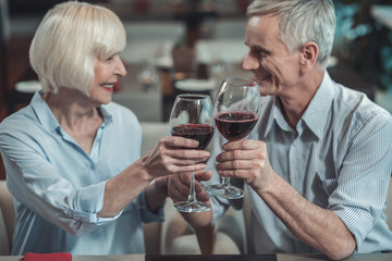 Pleasant relations. Delighted mature woman keeping smile on her face while going to drink wine