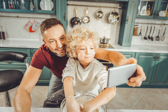 Grey phone. Dark-haired good-looking father using his grey smart phone for making photo with son