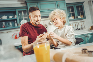 Baking rings. Curly blonde-haired boy feeling excited while giving baking rings his father cooking pie together