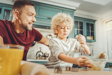 Bearded father. Bearded father wearing dark red shirt watching his son whipping baking mix