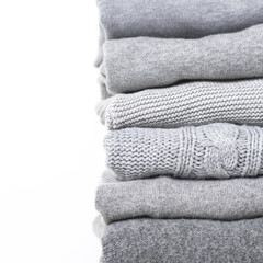 Careful stack of grey woolen and cashmere sweaters on white background