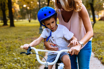 Obraz premium Mother helps her son to ride a bike