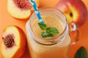 Smoothies made from ripe peaches in a glass jar with mint and fruits on a wooden table, close-up