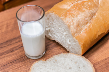 A glass of milk and bread on a wooden table.