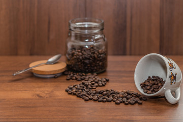 A cup of coffee and coffee beans, standing on a wooden table.