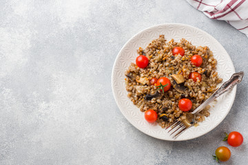 Buckwheat porridge with mushrooms and cherry tomatoes on a plate. Copy space