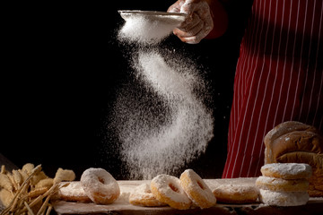 Chef hands sprinkling preparing bread dough and doughnuts with icing sugar on wooden table isolated...