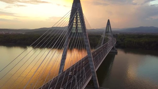 Budapest, Hungary - 4K flying away from Megyeri Bridge at sunset with heavy afternoon traffic with golden sky and Buda Hills at background
