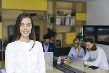 Fototapeta premium Young businesswoman standing in the office and other young business people working in the background