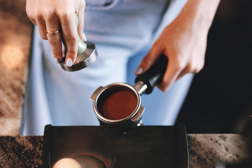 A young pretty slim girl,wearing casual outfit,is cooking coffee in a modern coffee shop. It focuses on the process.