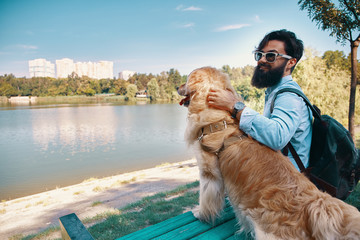 Young man sitting with his dog on the chair in the park, enjoyin