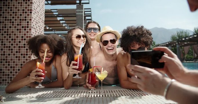 Guy filming a video of his friends in swimming pool drinking cocktails and chatting. always online 4k
