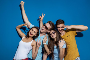 Four good-looking friends are laughing while standing in front of the blue wall having confident...