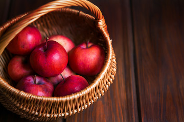 Red apples in a wicker basket on dark wooden boards