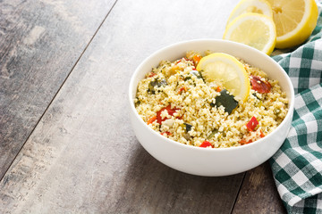 Couscous with vegetables in bowl on wooden table. Copyspace