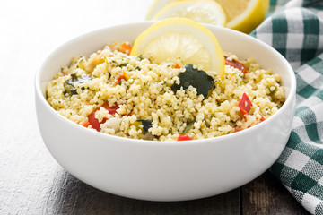 Couscous with vegetables in bowl on wooden table. 