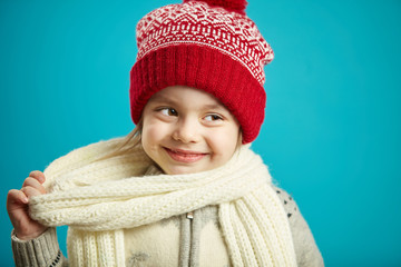 Little girl in beautiful red hat and scarf stands on blue isolated background, close-up portrait