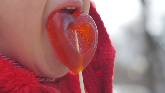 Cute little girl closeup funny licking a sweet lollipop in the shape of heart