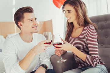 Pleasant time spending. Portrait of young charming lovers looking ta each other while clanging wine glasses and expressing true feelings