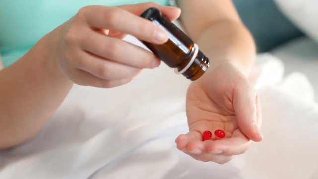 Slow motion video of sick woman lying in bed and pouring pills on hand from glass container