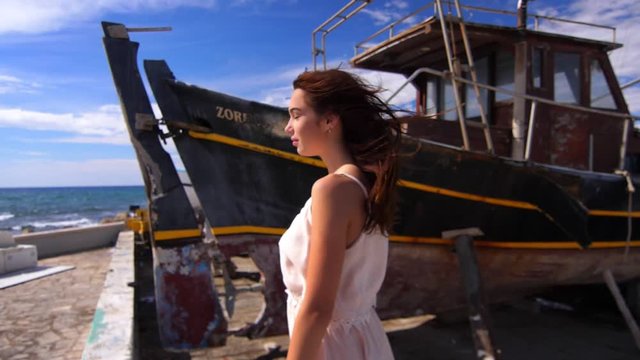 Sensual woman on sea coast enjoy windy weather. Brunette woman posing for camera near sea ship. Summer model on seashore. Female model near old ship. Beauty girl with wind hair