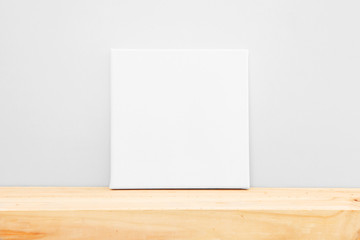 Mockup poster frame. White square canvas on wooden table.