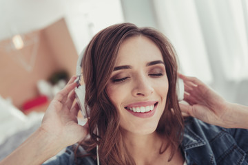 Pleasant moments. Close up of young stylish girl wearing earphones and listening to splendid music while keeping her eyes closed and touching her head