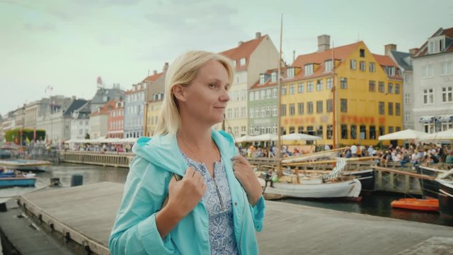 A woman strolls along the Nyhavn canal, against the background of famous colorful houses. The most popular place among tourists is in Copenhagen, Denmark