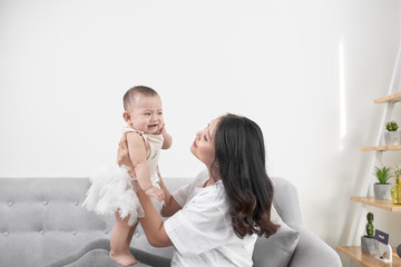 Mother and baby laugh together at home. They are sitting on the sofe in a brightly lit living room at the weekend together, lazy morning, warm and cozy scene. Selective focus