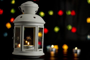 Christmas white lantern with a burning candle on the background of colorful lights garland, bokeh.
