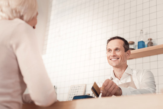 Professional service. Smart cheerful man looking at his customer while taking payment for the order