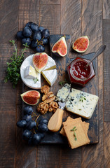 Cheese plate with grapes, figs, crackers, honey, plum jelly, thyme and nuts, top view.
