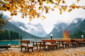 Naklejka premium Dobbiaco Lake or Toblacher in Dolomites with wooden tables and benches in outdoor cafe restaurant in autumn