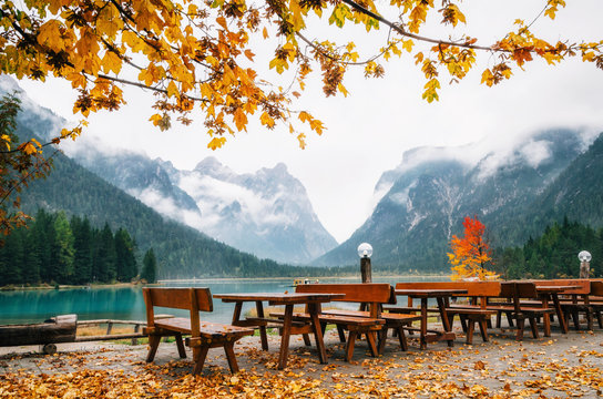 Dobbiaco Lake or Toblacher in Dolomites with wooden tables and benches in outdoor cafe restaurant in autumn