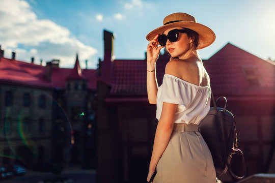 Young stylish woman wearing hat and sunglasses outdoors. Stylish girl with backpack and phone walking in Lviv