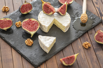 Brie cheese with fresh figs, honey and nuts. On shale plate and wooden background.