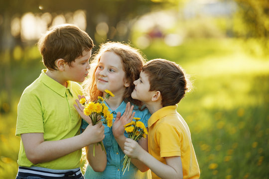 Little boys give his girl friend bouqet of yellow dandelions, springtime outdoors background.