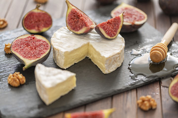 Brie cheese with fresh figs, honey and nuts. On shale plate and wooden background.