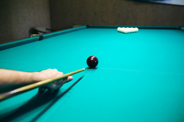 Man is playing billiard. Guy is holding pool cue in his hand. Small black cue ball is on the centre of the green table. Sports and indoor games free time concept.