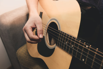 Man at home is playing the guitar. Guys hands are taking the chord on strings. Music making...