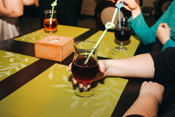 People are drinking cocktails in the cafe at the table. Woman is holding glass with a colourful straw in her hand. Evening out with friends. Chill out in summer.
