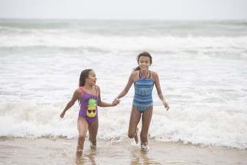 Two mixed-race sisters playing and laughing having fun on the beach on a bright tropical summer holiday