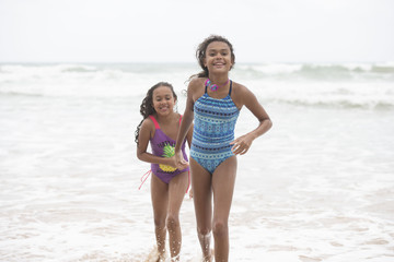 Two mixed-race sisters playing and laughing having fun on the beach on a bright tropical summer holiday