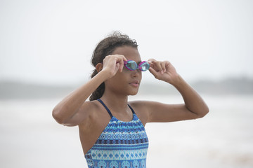 Beautiful curly haired mixed race pre-teen child in swim wear with  her swimming goggles about to start a swim